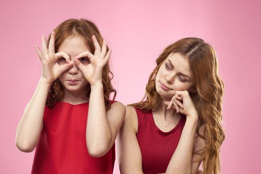 Mom and daughter in red dresses hugs fun grimace childhood joy pink background. High quality photo