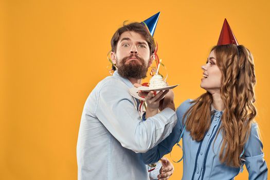 Man and woman at a party in caps and with tinsel cake fun yellow background. High quality photo