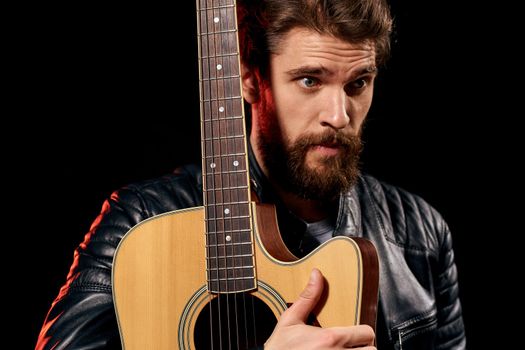 A man with a guitar in his hands leather jacket music performance rock star modern style dark background. High quality photo