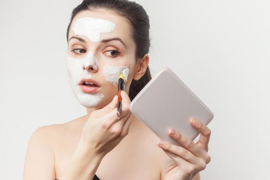 brunette holding makeup brush skin care face cream bare shoulders. High quality photo