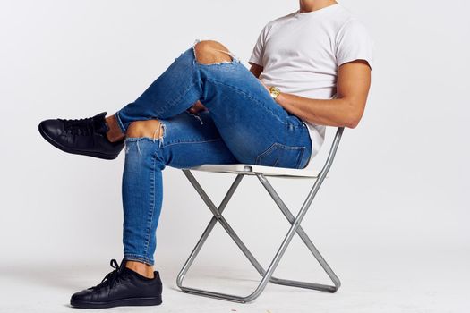a man in jeans and a t-shirt sits on a chair on a light background side view. High quality photo