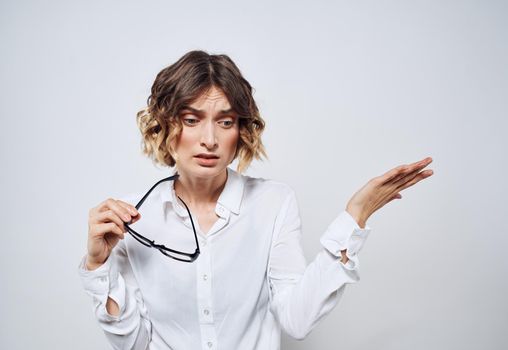 A beautiful woman in a white shirt holds glasses in her hands on a light background. High quality photo