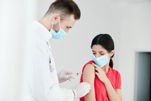 male doctor in a medical mask injections in the shoulder of a woman health coronavirus. High quality photo