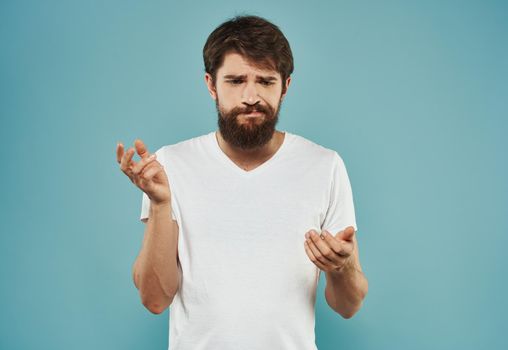 A brunette guy with a thick beard on a blue background gestures with his hands cropped view. High quality photo