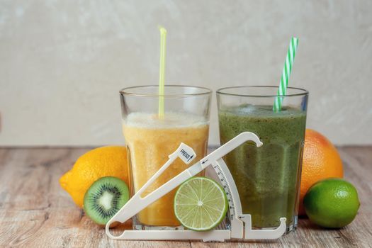 Tall glasses of kiwi and spinach smoothies in a row surrounded by fruits and caliper on a wooden table. The concept of losing weight and proper nutrition.