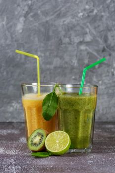Two tall glasses of orange juice and a banana-orange kiwi and spinach smoothie surrounded by fruit halves on a gray concrete background. The concept of losing weight and proper nutrition.