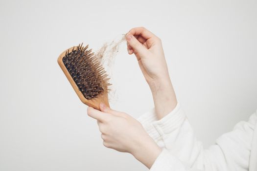 woman removes a bun of hair with a wooden comb on a light background health problems loss. High quality photo