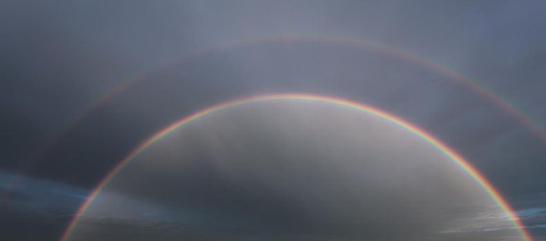 Nature background. Double rainbow in the sky against dark dramatic clouds