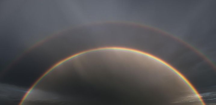 Nature background. Double rainbow in the sky against dark dramatic clouds