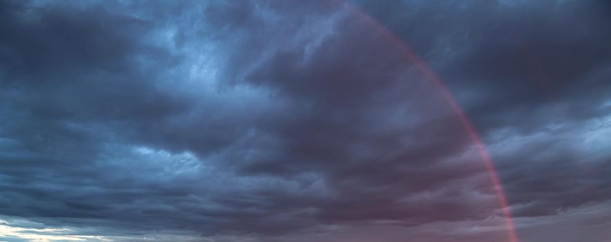 Rainbow in the sky against dark dramatic clouds 