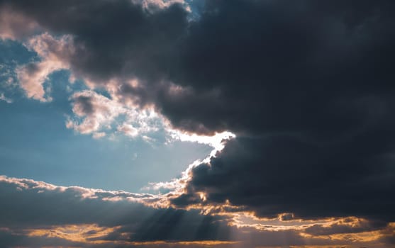 Sun rays shining through dark rainy clouds sky