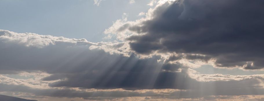 Sun rays shining through dark rainy clouds sky