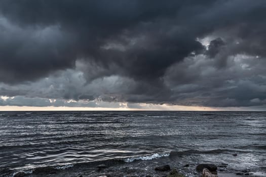 Amazing dramatic landscape. Dramatic dark clouds during sunset at sea. Dark sea water and heavy beautiful grey clouds.