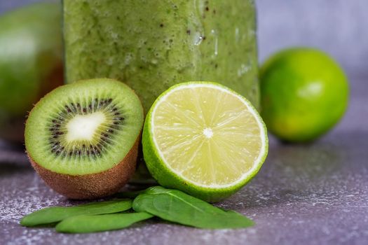Close-up of fresh kiwi and lime fruit halves against a smoothie mug on a gray concrete backdrop. The concept of a healthy lifestyle and proper nutrition. Good for your health. Vitamin drink.