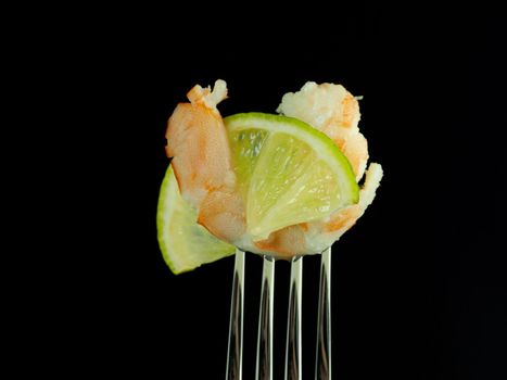 The kings shrimp on a fork with lime, on a black background. High quality photo