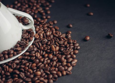 inverted white cup on a platter and sprinkled coffee beans on a dark background. High quality photo