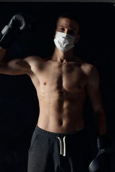 athlete in a medical mask and a pumped-up torso with boxing gloves on a black background. High quality photo