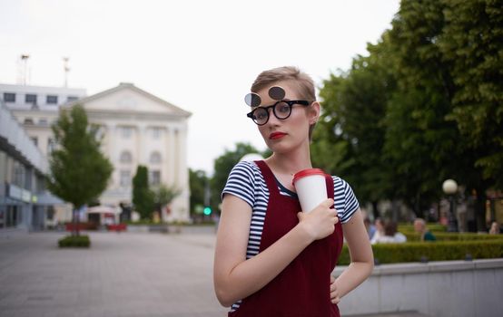 fashionable woman in a sundress and glasses on her face street nature summer trees building. High quality photo