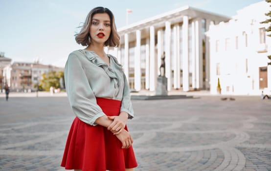 woman with bright makeup in a shirt and in a red skirt are walking on the street in summer near the building. High quality photo