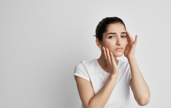 A woman in a white t-shirt holds her face with a headache and nigative health. High quality photo