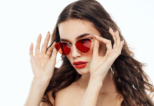 Brunette woman straightens glasses on her face and naked shoulders light background. High quality photo