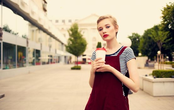 happy woman in a sundress walks down the street in nature with a cup of coffee in hand. High quality photo