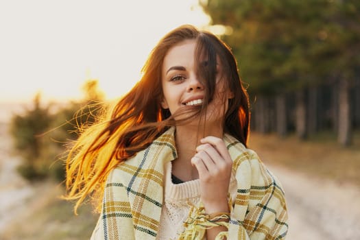 Woman with a plaid on her shoulders at sunset near the trees on the road. High quality photo