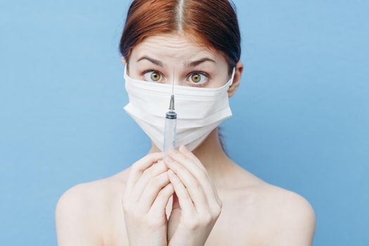 woman with syringe in hand and medical mask injection blue background. High quality photo