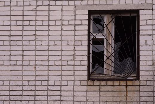 A broken window in a brick house. Broken glass in a window with a metal grate.