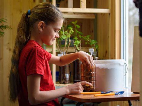 Girl pouring soil into a plastic bottle for planting seedlings of garden plants