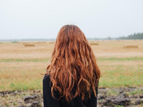 Beautiful woman with red hair in a black dress outdoors in the field. High quality photo