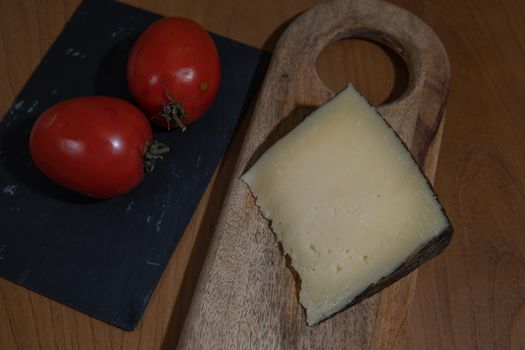 Cheese wedge with tomato on wooden plank