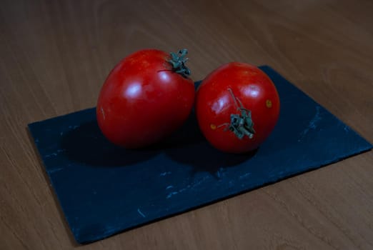 Natural red tomatoes on a black slate and wood background