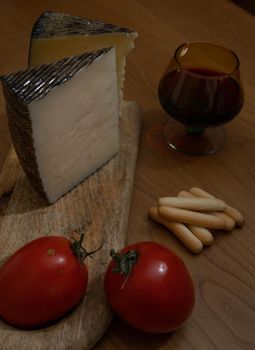 Cheese wedge with tomato, bread sticks and red wine