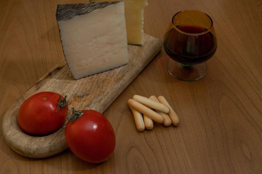 Cheese wedge with tomato, bread sticks and red wine