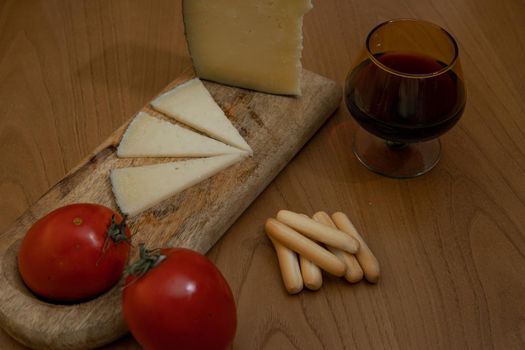 Cheese wedge with tomato, bread sticks and red wine