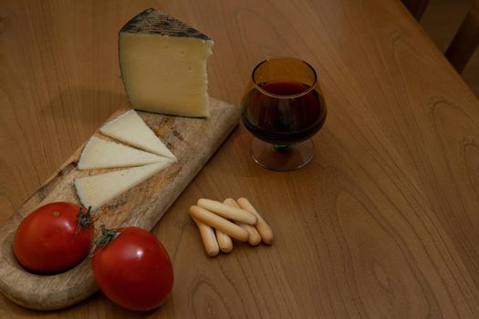 Cheese wedge with tomato, bread sticks and red wine