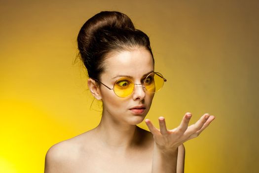 pretty woman in yellow glasses naked shoulders gestures with hands emotions. High quality photo