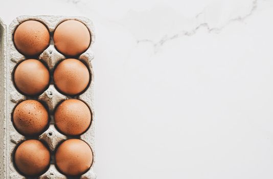 organic eggs in egg box on white marble kitchen table, closeup