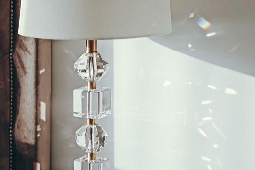 Gold and crystal details of a bedside lamp with shadows at sunset, luxury home decor closeup