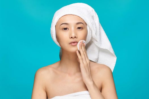 woman of asian appearance naked shoulders clear skin cotton pad blue background. High quality photo