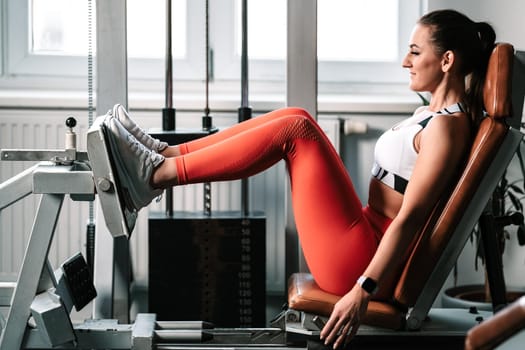 Exercising legs on machine in gym, female fitness instructor.