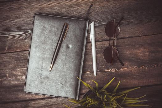 notepad glasses and a flower in a pot on a wooden table top view pen office. High quality photo