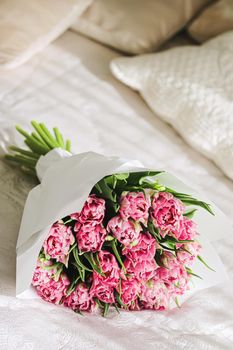 Romantic bouquet of pink tulips on bed in bedroom, holiday gift concept
