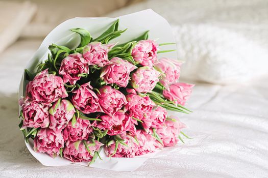 Romantic bouquet of pink tulips on bed in bedroom, holiday gift concept