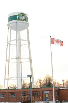 SMITHS FALLS, ONTARIO, CANADA, MARCH 10, 2021: A view of the Smiths Falls Watertower and Canadian Flag shot from the Beckwith St Bridge area in the small town.