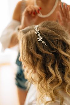 Stylist puts on a hairpin in the bride's hairstyle during wedding preparations . High quality photo