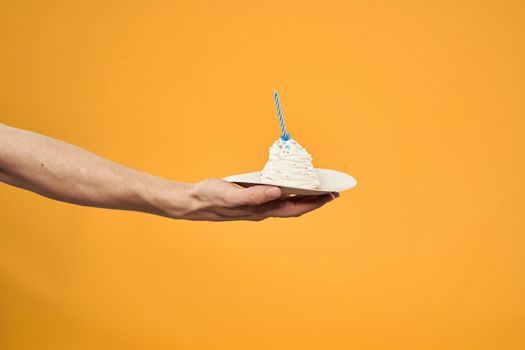 Cake with a candle in a man's hand on a yellow background cropped view Copy Space. High quality photo