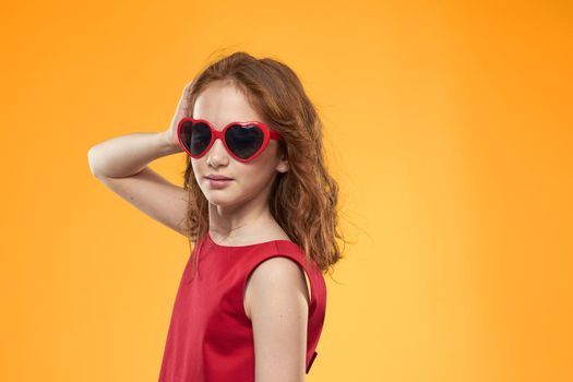 Girl in black glasses red dress childhood fun yellow background. High quality photo