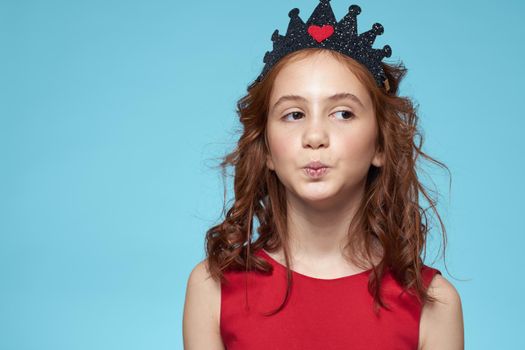 little girl with curly hair with a crown on her head red dress Smile blue background. High quality photo